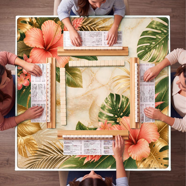 K&ouml;nnte beinhalten: Ein quadratischer Mahjong-Spieltisch mit tropischem Blumendesign. Der Tisch zeigt gro&szlig;e orangefarbene Hibiskusbl&uuml;ten, gr&uuml;ne Monstera-Bl&auml;tter und goldfarbene Akzente. Vier Personen spielen, ihre H&auml;nde sind sichtbar.