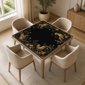 Op de afbeelding: Een vierkante eettafel met een zwart tafelblad voorzien van een decoratieve rand met gouden luipaarden, bamboestengels en gele bloemen. De tafel is omringd door vier lichtbeige gestoffeerde fauteuils met houten poten op een licht kleed.