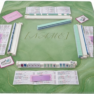 May include: A complete Mahjong set on a green marble-patterned mat. The set includes tiles, racks, dice, and score cards. The word "[NAME]" is embossed on the mat. The tiles are green and white.