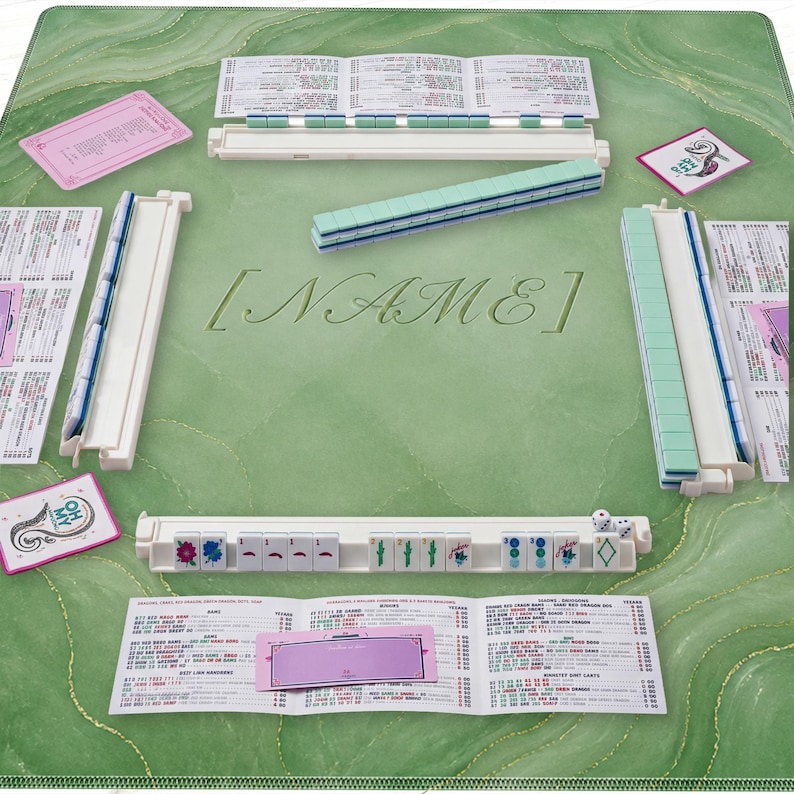 May include: A complete Mahjong set on a green marble-patterned mat. The set includes tiles, racks, dice, and score cards. The word "[NAME]" is embossed on the mat. The tiles are green and white.