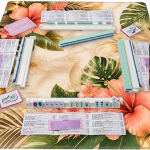 K&ouml;nnte beinhalten: Ein Mahjong-Set mit wei&szlig;en und t&uuml;rkisfarbenen Spielsteinen, W&uuml;rfeln und Spielanleitungen. Das Set ist auf einer floral gemusterten Matte mit rosa Hibiskusbl&uuml;ten und gr&uuml;nen Bl&auml;ttern angeordnet. Die Spielsteine sind ordentlich angeordnet.