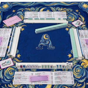 Könnte beinhalten: Ein komplettes Mahjong-Set mit einer blauen Spielfläche mit Sternennacht-Design. Das Set enthält Spielsteine, Racks und Wertungskarten. Das zentrale Design ist ein stilisiertes "A" mit einem Mond.