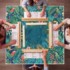 May include: A square Mahjong game table with a tropical design featuring parrots, toucans, and lush foliage. The table is surrounded by players, with wooden racks holding tiles and score sheets. The color palette includes teal, green, and pops of red and yellow.