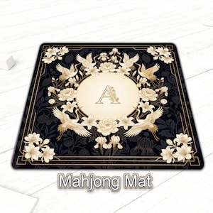 Könnte beinhalten: Rechteckige Mahjong-Matte mit schwarzem Hintergrund und goldenem Rand. Die Matte zeigt ein zentrales ovales Design mit dem Buchstaben "A", umgeben von Blumen und Kranichen. Die Worte "Mahjong Mat" stehen unten.