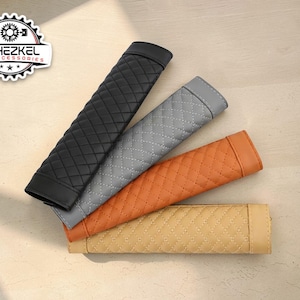 May include: Four car seat belt covers in black, gray, orange, and tan. Each cover has a diamond-stitched pattern. The covers are arranged diagonally on a light-colored surface. The logo "YEHEZKEL CAR ACCESSORIES" is in the upper left corner.