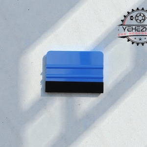 Könnte beinhalten: Blauer Abzieher mit schwarzer Gummikante für die Autopflege. Das Werkzeug hat eine rechteckige Form und befindet sich vor einem weißen Hintergrund. Das Logo "YEHEZKEL CAR ACCESSORIES" ist oben rechts sichtbar.