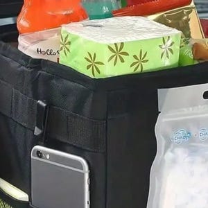 Peut inclure: Organisateur de voiture noir avec plusieurs compartiments, contenant divers articles. Comprend un smartphone dans une poche lat&eacute;rale, une bo&icirc;te de mouchoirs, des collations et des boissons. Con&ccedil;u pour &ecirc;tre suspendu au si&egrave;ge de la voiture.
