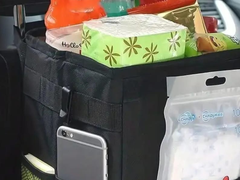 Peut inclure: Organisateur de voiture noir avec plusieurs compartiments, contenant divers articles. Comprend un smartphone dans une poche lat&eacute;rale, une bo&icirc;te de mouchoirs, des collations et des boissons. Con&ccedil;u pour &ecirc;tre suspendu au si&egrave;ge de la voiture.