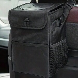 Peut inclure: Sac poubelle de voiture noir avec fermeture &agrave; rabat et poche en filet. Le sac est suspendu &agrave; l'appuie-t&ecirc;te d'un si&egrave;ge de voiture. Le sac a une ouverture circulaire sur le dessus et une sangle &agrave; boucle.