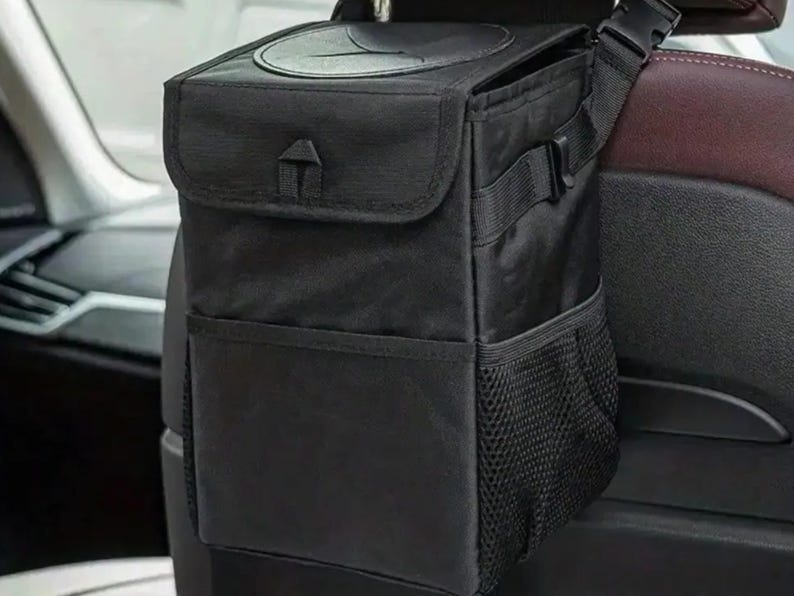Peut inclure: Sac poubelle de voiture noir avec fermeture &agrave; rabat et poche en filet. Le sac est suspendu &agrave; l'appuie-t&ecirc;te d'un si&egrave;ge de voiture. Le sac a une ouverture circulaire sur le dessus et une sangle &agrave; boucle.