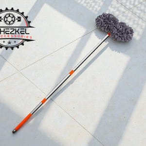 Puede incluir: Un plumero para coche con cabezal de microfibra gris y mango extensible plateado y naranja. El plumero está diseñado para limpiar vehículos. El logotipo "YEHEZKEL CAR ACCESSORIES" es visible.