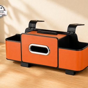 Könnte beinhalten: Ein orangefarbener und schwarzer Auto-Organizer mit einem Taschentuchhalter und zwei Seitenfächern. Der Organizer hat ein schlankes Design mit silberner Zierleiste um die Taschentuchöffnung und besteht aus lederähnlichem Material. Er hat zwei schwarze Griffe.