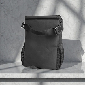 Peut inclure: Un sac &agrave; d&eacute;jeuner isotherme noir avec une bandouli&egrave;re et une poche lat&eacute;rale en filet. Le sac a une fermeture &agrave; enroulement et une boucle. Le sac est con&ccedil;u pour garder les aliments et les boissons au frais. Le sac est pos&eacute; sur une surface blanche.