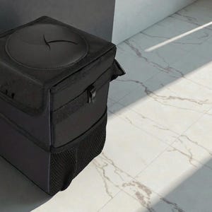 Peut inclure: Une poubelle de voiture noire et rectangulaire avec un couvercle dot&eacute; d'une ouverture circulaire. La poubelle a une poche en filet en bas et une fermeture &agrave; boucle. L'article est fait d'un tissu fonc&eacute; durable.