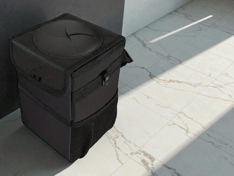 Peut inclure: Une poubelle de voiture noire et rectangulaire avec un couvercle dot&eacute; d'une ouverture circulaire. La poubelle a une poche en filet en bas et une fermeture &agrave; boucle. L'article est fait d'un tissu fonc&eacute; durable.