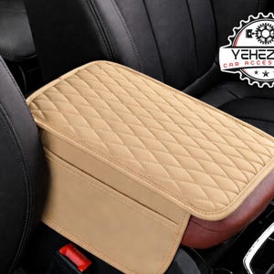 Könnte beinhalten: Beige gesteppte Autoarmlehne mit Rautenmuster. Die Armlehne hat eine braune Basis und eine Tasche auf der Vorderseite. Das Logo "YEHEZKEL CAR ACCESSORIES" ist im Hintergrund sichtbar.
