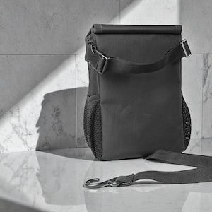 Peut inclure: Un sac &agrave; d&eacute;jeuner isotherme noir avec une fermeture &agrave; enroulement et une bandouli&egrave;re. Le sac a une poche lat&eacute;rale en filet et une fermeture &agrave; boucle. La sangle est d&eacute;tach&eacute;e et pos&eacute;e sur la surface.