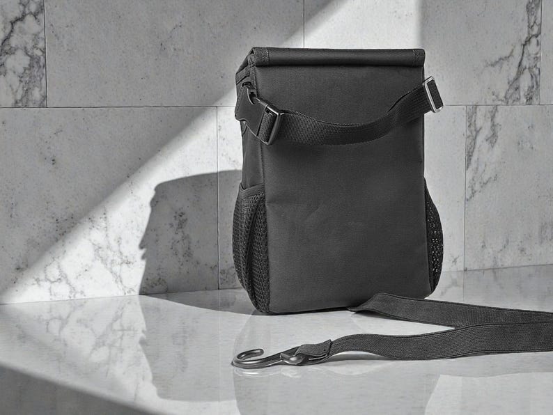 Peut inclure: Un sac &agrave; d&eacute;jeuner isotherme noir avec une fermeture &agrave; enroulement et une bandouli&egrave;re. Le sac a une poche lat&eacute;rale en filet et une fermeture &agrave; boucle. La sangle est d&eacute;tach&eacute;e et pos&eacute;e sur la surface.