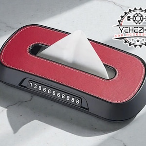 Könnte beinhalten: Rote und schwarze Auto-Taschentuchbox mit einem weißen Taschentuch, das aus der Oberseite herausragt. Die Taschentuchbox hat eine Zahlenanzeige und den Text "YEHEZKEL CAR ACCESSORIES".