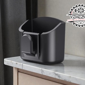 Könnte beinhalten: Ein schwarzer Auto-Zubehör-Organizer mit gewölbter Oberseite und Clip an der Seite. Der Organizer steht auf einer weißen Marmorarbeitsplatte. Das Logo "YEHEZKEL CAR ACCESSORIES" ist oben rechts sichtbar.