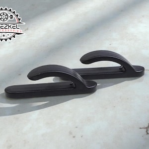 Könnte beinhalten: Zwei schwarze Autozubehörteile mit gebogenem Griffdesign. Die Zubehörteile bestehen aus einem haltbaren Material und sind für die Befestigung an einem Fahrzeug konzipiert. Das Logo "YEHEZKEL CAR ACCESSORIES" ist sichtbar.