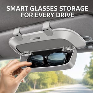 May include: A light gray car visor glasses case with a hinged lid, containing a pair of black sunglasses. The text SMART GLASSES STORAGE FOR EVERY DRIVE is printed above the case, which is attached to a vehicle sun visor.