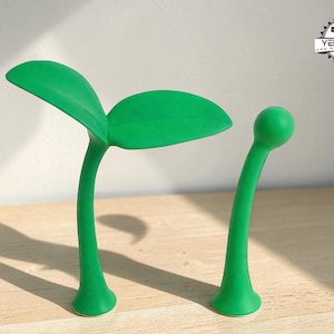 以下が含まれることがあります： 2つの明るい緑色の、様式化された植物型のオブジェクト。1つは2枚の葉、もう1つは単一の球状の頂点があります。どちらも湾曲した茎と丸みを帯びた基部を持っています。オブジェクトは明るい色の表面にあり、右上にロゴがあります。