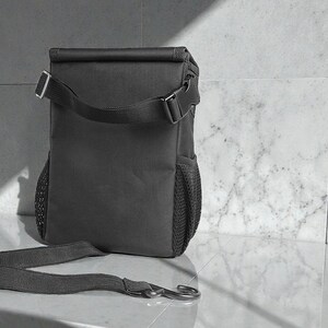 Peut inclure: Un sac &agrave; lunch isotherme gris fonc&eacute; avec une bandouli&egrave;re et une poche lat&eacute;rale en filet. Le sac a une fermeture &agrave; enroulement avec une boucle et un crochet en m&eacute;tal argent&eacute;.
