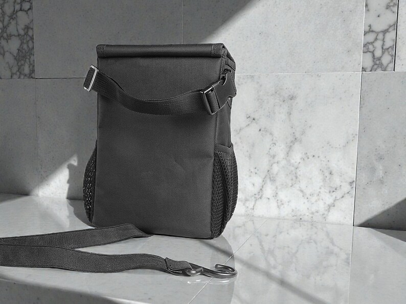 Peut inclure: Un sac &agrave; lunch isotherme gris fonc&eacute; avec une bandouli&egrave;re et une poche lat&eacute;rale en filet. Le sac a une fermeture &agrave; enroulement avec une boucle et un crochet en m&eacute;tal argent&eacute;.
