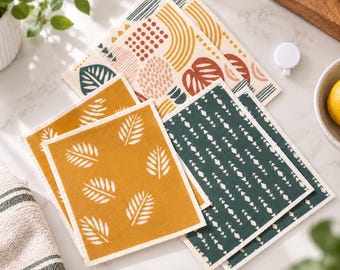 Peut inclure: Un ensemble de lavettes suédoises rectangulaires présentant divers motifs, notamment jaune moutarde avec des feuilles blanches, vert foncé avec des losanges géométriques blancs, et un fond crème avec des formes abstraites moutarde, rouge et vert.