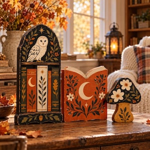 May include: A set of three wooden decorative items featuring a tall arched piece with a white owl, a book-shaped piece with a crescent moon, and a mushroom-shaped piece, all painted in black, orange, and white with floral and leaf motifs.