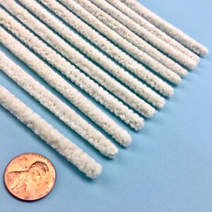 May include: A collection of off-white chenille stems, or pipe cleaners, displayed diagonally against a light blue backdrop. A penny is included for scale. These craft items are commonly used for various arts and crafts projects.