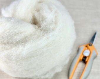 May include: A white ball of wool fiber, ready for felting, next to a pair of orange and gray handled scissors.