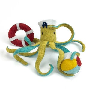 May include: A yellow felt octopus wearing a blue and white sailor hat, holding a red and white life preserver and a multi-colored beach ball.