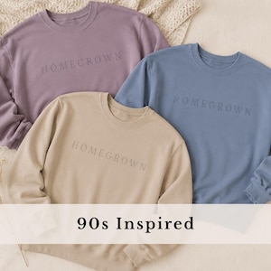 May include: Three crewneck sweatshirts in mauve, blue, and beige, each featuring the word HOMEGROWN embroidered in a matching thread color across the chest. The garments have long sleeves, ribbed cuffs, and a classic fit, with 90s Inspired text.