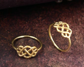 May include: Two gold rings featuring Celtic knot designs. The rings are set against a dark, textured background. The rings display an intricate, interwoven pattern, reflecting a classic and elegant style. The rings are likely made of metal.