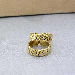 May include: Two gold-colored adjustable rings with a textured, dotted pattern. The rings are stacked on top of each other, showcasing their design. The rings are made of metal and are likely costume jewelry.