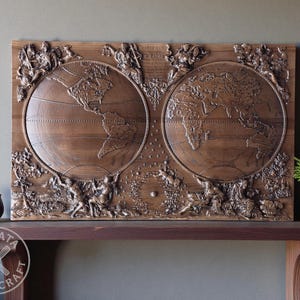May include: A detailed wooden world map carving. The map shows the continents within two circular frames, with elaborate relief carvings of figures and foliage. The wood has a warm, brown colour. The piece is displayed on a dark brown shelf.