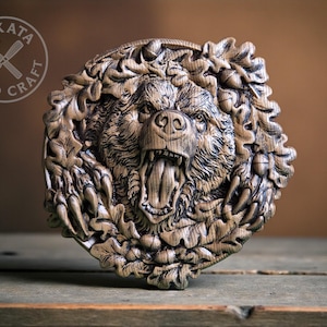 Könnte beinhalten: Runde Holzskulptur eines brüllenden Bärenkopfes, umgeben von geschnitzten Blättern. Die Details des Fells und der Zähne sind fein ausgearbeitet. Der Text "BUKATA WOOD CRAFT" ist kreisförmig angeordnet. Naturholz-Finish.