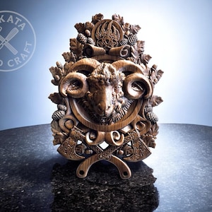 May include: A detailed wooden carving of a ram's head with curved horns, surrounded by foliage, pine cones, and crossed axes. The carving has a natural wood finish, possibly a decorative wall hanging or plaque.