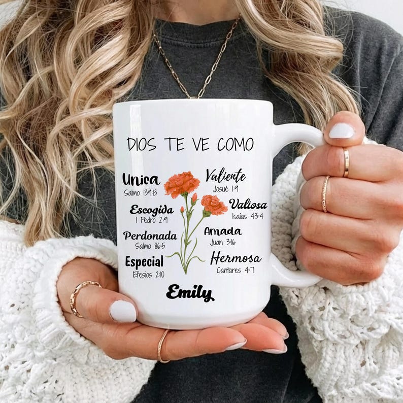 Peut inclure: Mug en c&eacute;ramique blanche avec le texte "DIOS TE VE COMO" et d'autres mots espagnols. La tasse pr&eacute;sente des illustrations de fleurs orange et le nom "Emily". La tasse a une anse et est tenue par une personne.