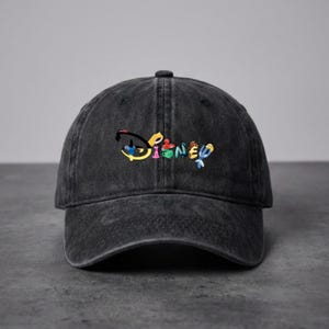 Op de afbeelding: Een zwarte, uitgewassen baseballcap met het Disney-logo geborduurd in kleurrijke letters. De cap heeft een gebogen klep en een stoffen bandsluiting aan de achterkant. Het Disney-logo is in een regenboog van kleuren.