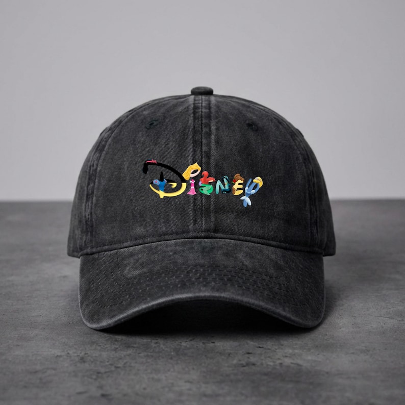 Op de afbeelding: Een zwarte, uitgewassen baseballcap met het Disney-logo geborduurd in kleurrijke letters. De cap heeft een gebogen klep en een stoffen bandsluiting aan de achterkant. Het Disney-logo is in een regenboog van kleuren.