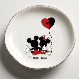 May include: White ceramic plate with a gold rim featuring Mickey and Minnie Mouse embracing. A red and black heart-shaped balloon floats above them. The names "Noah" and "Sarah" are printed below the characters.