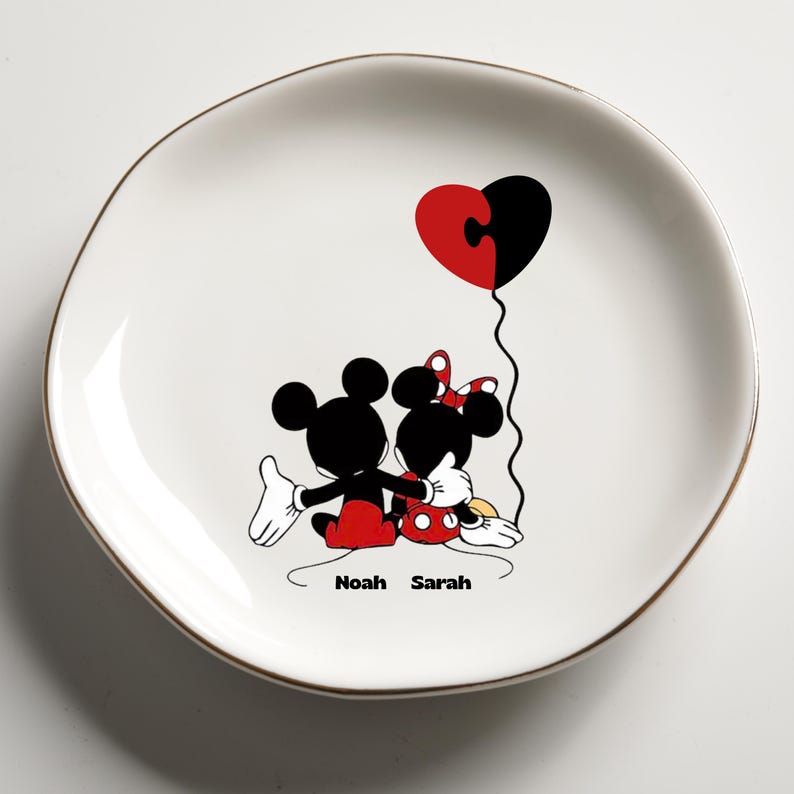 May include: White ceramic plate with a gold rim featuring Mickey and Minnie Mouse embracing. A red and black heart-shaped balloon floats above them. The names "Noah" and "Sarah" are printed below the characters.