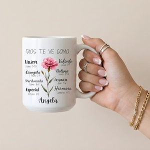 Peut inclure: Mug en c&eacute;ramique blanche avec le texte "DIOS TE VE COMO" et d'autres mots espagnols. Une illustration de fleur rose est sur le c&ocirc;t&eacute; gauche. Le mug est tenu par une personne avec plusieurs bagues et un bracelet dor&eacute;.