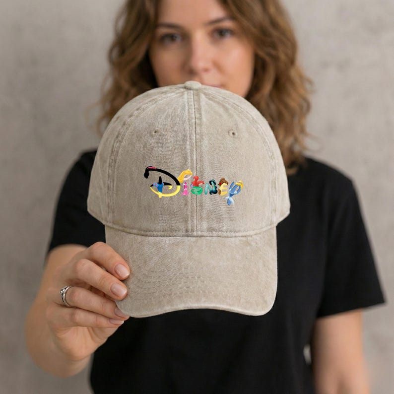 May include: A tan baseball cap with the embroidered word "Disney" in colorful letters. The hat has a curved brim and an adjustable strap at the back. The cap is made of a soft, worn material.