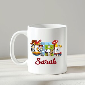 May include: White ceramic mug featuring the word "GIRL" in colorful, cartoon-style letters with a "Toy Story" theme. The name "Sarah" is written in red script below the word "GIRL".