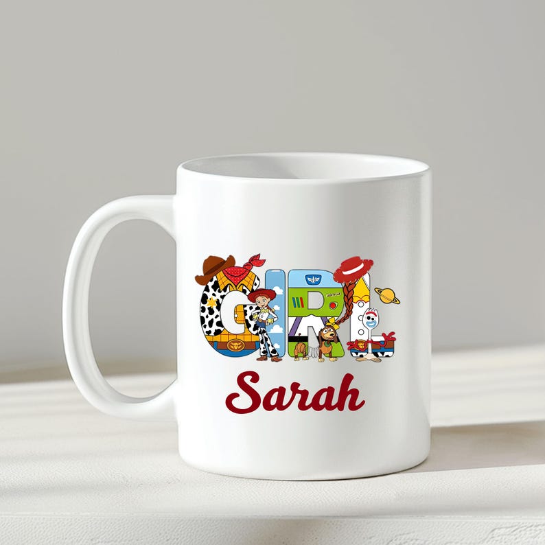 May include: White ceramic mug featuring the word "GIRL" in colorful, cartoon-style letters with a "Toy Story" theme. The name "Sarah" is written in red script below the word "GIRL".
