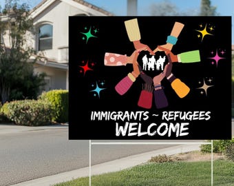 May include: A black yard sign with the words "IMMIGRANTS ~ REFUGEES WELCOME" in white. The sign features a graphic of hands forming a heart shape around silhouettes of people. Colorful starbursts are scattered around the hands.